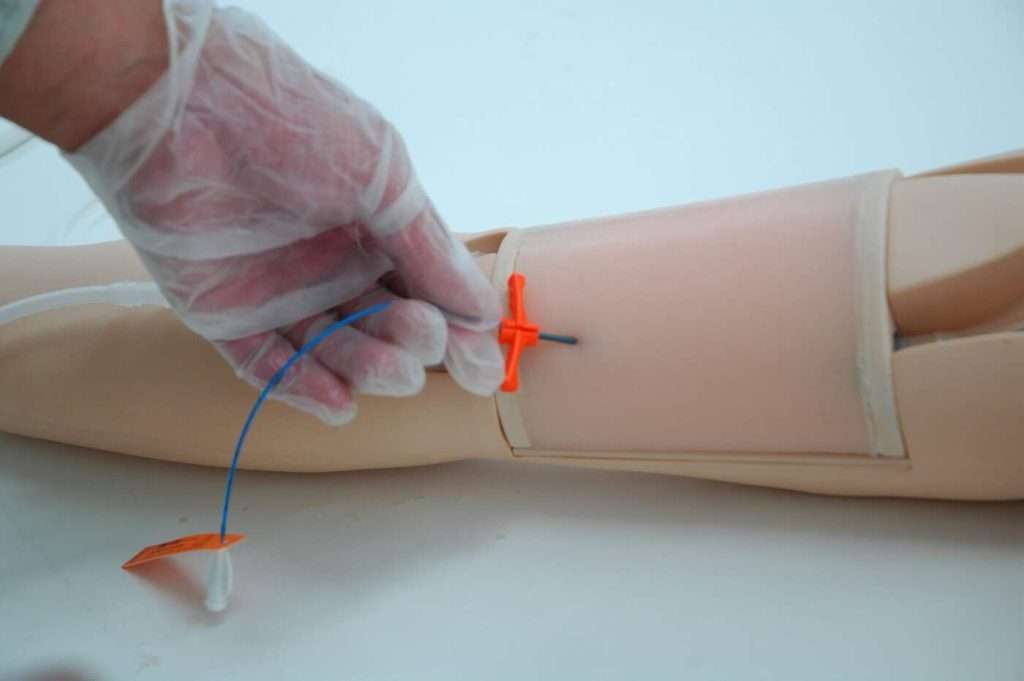 person inserting PICC line into the arm of a patient simulator