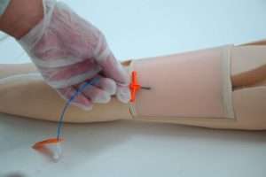 person inserting PICC line into the arm of a patient simulator